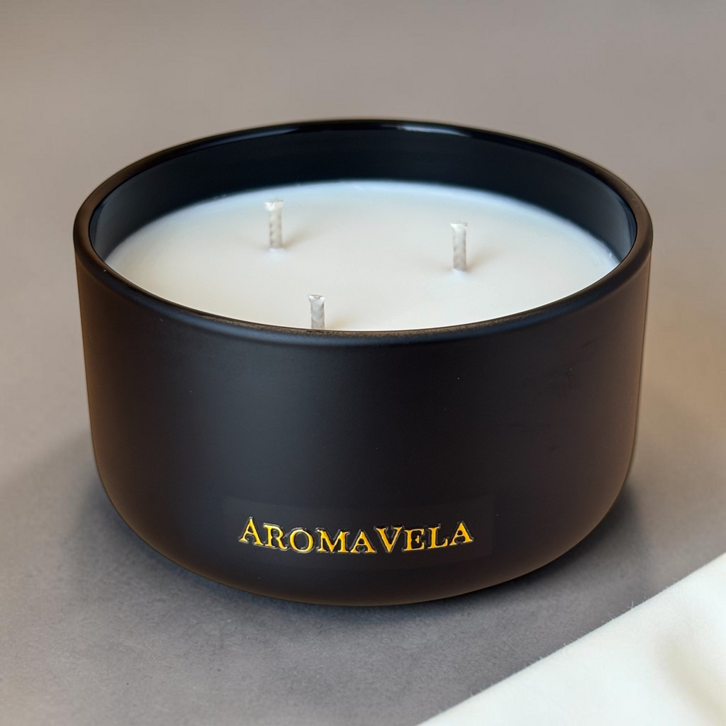Black candle with three wicks on a neutral background, featuring the brand 'Aromavela'.